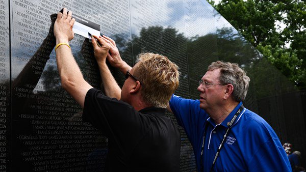 A volunteer helps a Vietnam Veteran trace the name of a comrade whom he lost in the war.