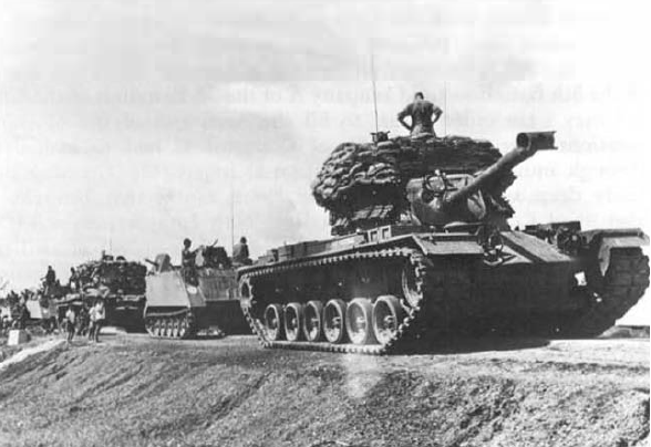 Photo of an M48A3 tank with protective sandbags followed by M113 ACAVs (U.S. Army)