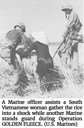 Photo of a Marine officer assisting a South Vietnamese woman as she gathers the rice into a shock while another Marine stands guard during Operation GOLDEN FLEECE. (U.S. Marines)