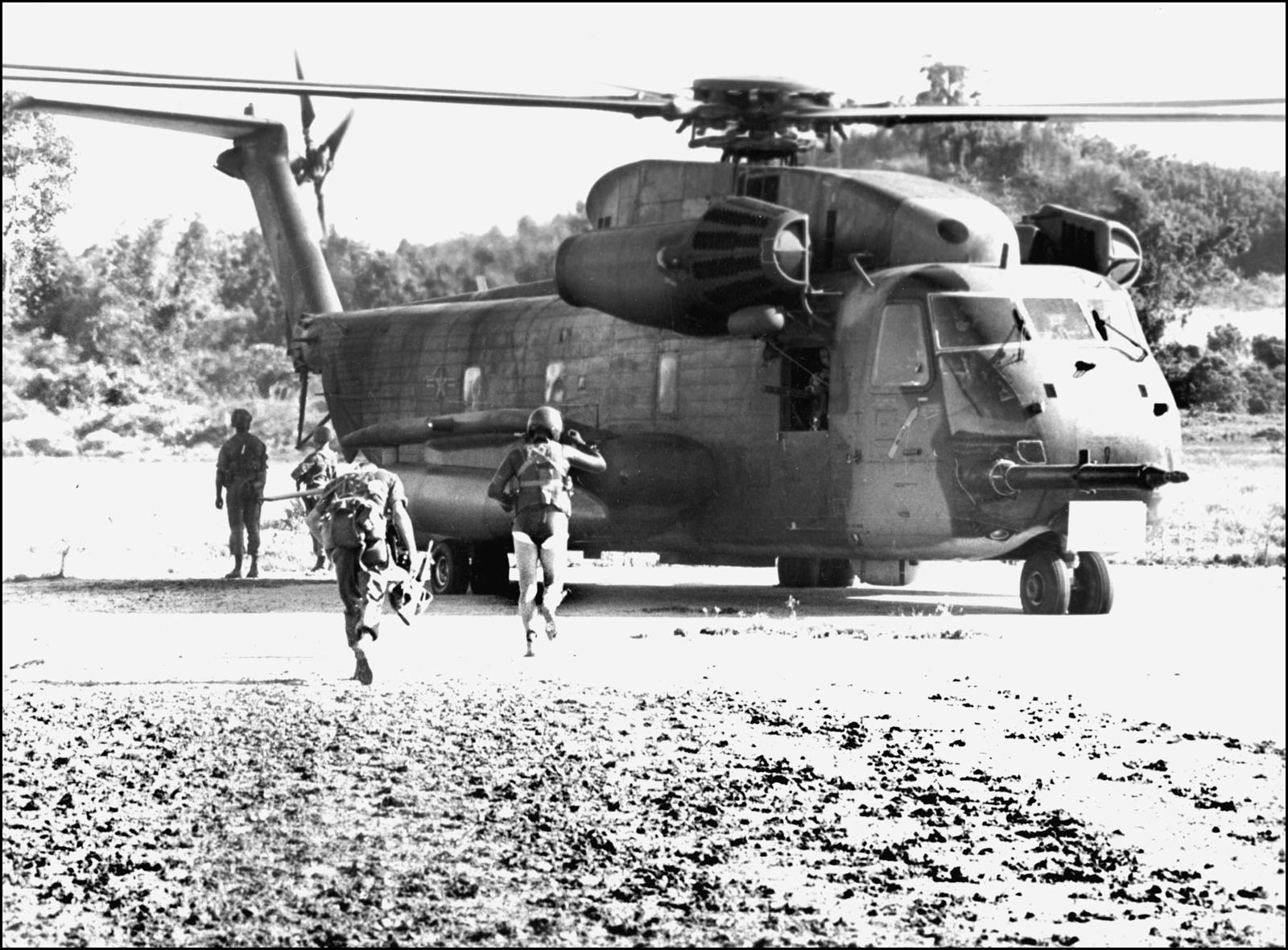Marines and Airmen on Koh Tang move toward a CH-53 Sea Stallion. 13 men were killed when one CH-53 was shot down just off the beach as the assault got underway. (U.S. Air Force)