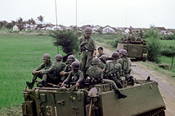 Vietnamese Popular Force soldiers riding on Australian APCs